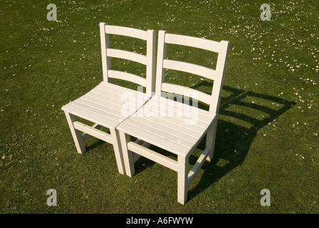 two wooden white chairs on a lawn covered with daisies Stock Photo