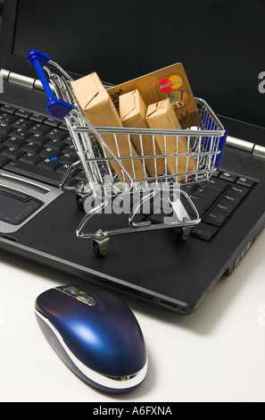 Online shopping, a shopping cart filled with parcel and a credit card standing on the keyboard of a notebook computer Stock Photo