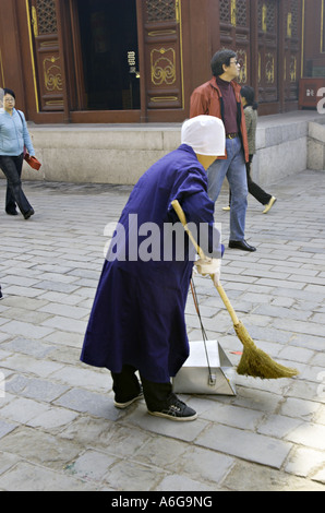 CHINA BEIJING Female Chinese sanitation worker wearing a blue coat and white cap sweeps up litter in Lama Temple Stock Photo