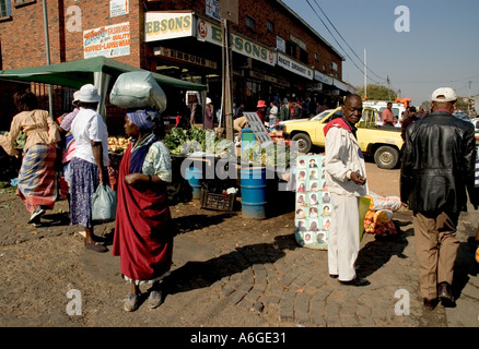 South Africa Johanesburg Alexandra Township woman with load on her head and people in the street with vegetable stall in bkgd Stock Photo