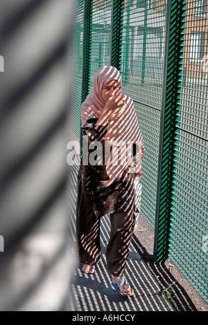 An asian girl walks past a fence in East London Stock Photo
