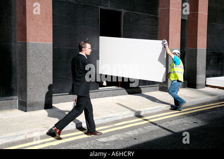 A man in a suit walks past a building site in London Stock Photo