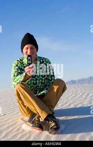 young man sitting on sand dune using mobile phone to text message Stock Photo