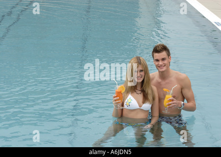 young pair standing in the water of a swimming pool up to the belly, holding soft drinks Stock Photo
