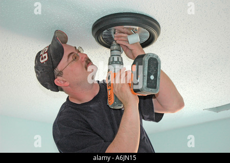 Electrician installing fans lights and circuit panels and breakers on ladders by hand Stock Photo
