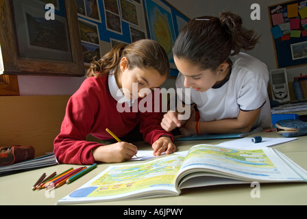 Junior girl students in school uniform 9-11 years working on a geography project together in school classroom with map book open in foreground Stock Photo