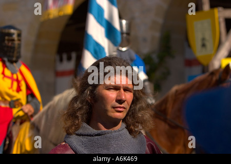 French Long haired man close up with medieval knights on horseback in background carrying banners at french medieval festival, south West France eu Stock Photo