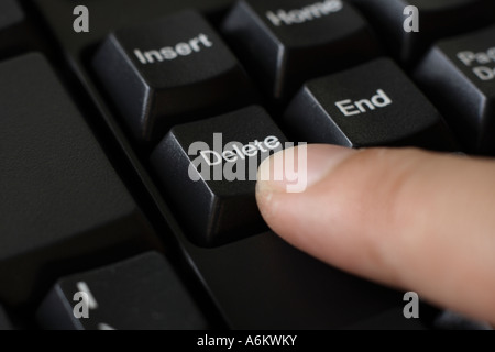 finger pressing delete button on black keyboard Stock Photo