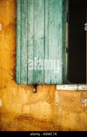 Green shutters against a yellow cracked and crumbling plaster wall, taken on Rhodes, Greece Stock Photo
