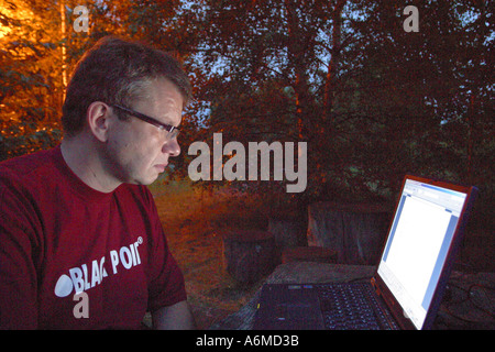 Man working on his laptop computer late at night under the trees in his garden Stock Photo