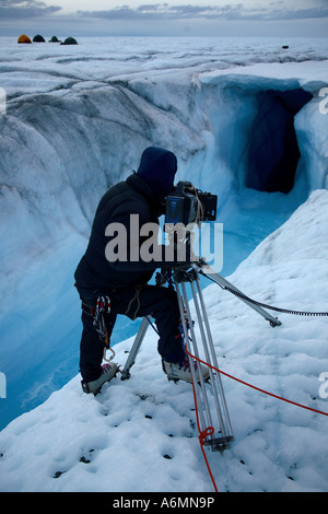 A freelance adventure cameraman at work on the Greenland ice shelf filming a Moulin Stock Photo