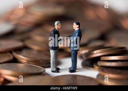 Business figures shaking hands surrounded by pennies. Stock Photo