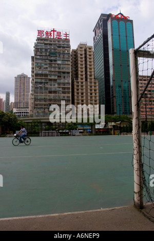 A man riding a bicycle across an empty football pitch in the centre of Hong Kong City Stock Photo