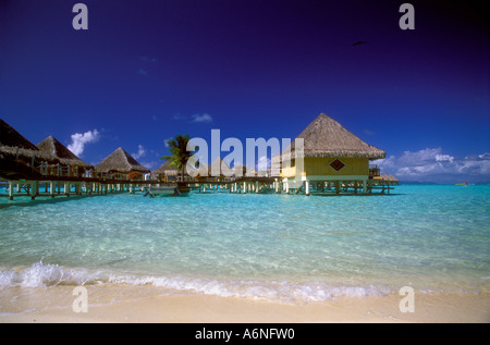 Thatched roofed bungalows of hotel over lagoon South Pacific Stock Photo