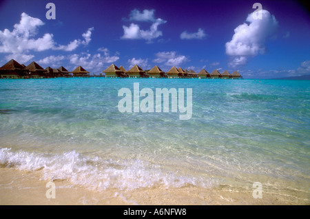 Thatched roof bungalows on horizon of crystal clear lagoon Stock Photo