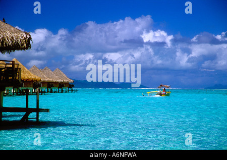 Thatched roof bungalows and yellow outrigger boat on horizon of crystal clear lagoon Stock Photo