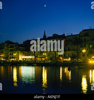 Night view along harbor waterfront with people dining in brightly lit restaurants and street lights reflecting in water Corsica Stock Photo