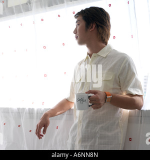 Man having a drink of coffee and looking out of a window Stock Photo