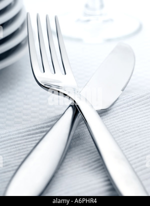 CLOSE UP OF A KNIFE AND FORK, WITH PLATES AND GLASS IN BACKGROUND Stock Photo