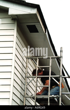 Carpenter working on aluminum access scaffold tower installing maintenance free plastic over cladding to eaves soffit board & timber fascia house UK Stock Photo