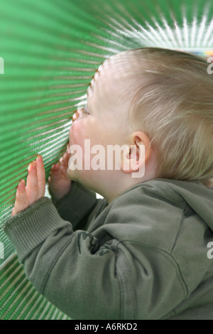 Child pressing face against green tunnel in playground enjoying touch Stock Photo