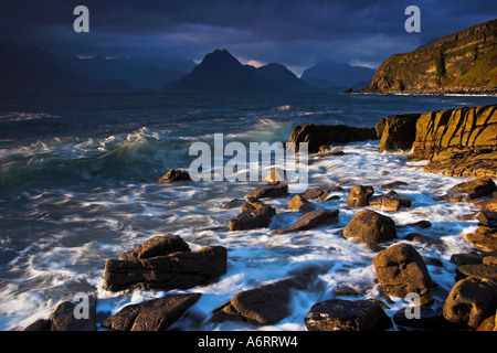 An ominous sky looms over the Cuillin Hills on the Isle of Skye.  On the rocky outcrop of Elgol, sunshine glows on the rocks Stock Photo