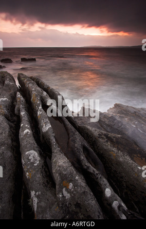 Alien shaped rocks isolate sea water at Elgol in Scotland.  The sunset burns beneath a heavy clouded sky Stock Photo