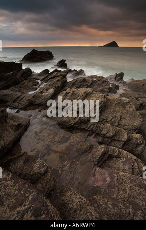 Sunset lights the cloudy sky above Wembury Bay in Devon.  The incoming tide laps around the rocky shore Stock Photo