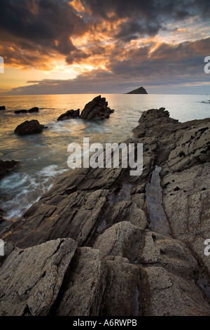 Sunset lights the cloudy sky above Wembury Bay in Devon.  The incoming tide laps around the rocky coast Stock Photo