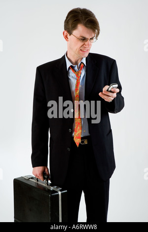 BUSINESS MAN IN DARK SUIT STRESSED HOLDING BRIEFCASE AND MOBILE PHONE TEXTING Stock Photo