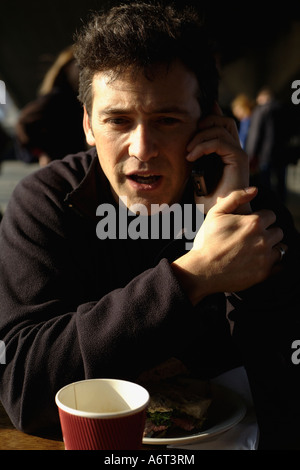 Man having lunch on mobile phone under Waterloo Bridge, South Bank, London, England, UK Stock Photo