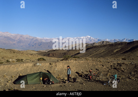 girl and tent with two bicycles camped on remote ridge at sunset with snowy peakes of Andes behind in Northern Argentina Stock Photo