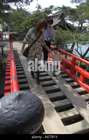 Japan Nothern Honshu Miyagi ken Matsushima bay couple and young child crossing a traditional red bridge with temple in bkgd Stock Photo