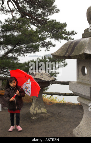 Japan Nothern Honshu Miyagi ken Matsushima bay young female child holding a red umbrella on rainy day with traditional stone sta Stock Photo