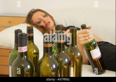 Young Woman Lying On Couch Holding Bottle Of Wine After Drinking Too Much Stock Photo