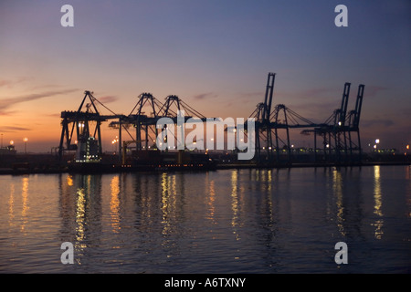 Silhouetted dockside cranes at sunrise with floodlights & mauve sky reflected in water at Port Kelang for Kuala Lumpur Malaysia Stock Photo