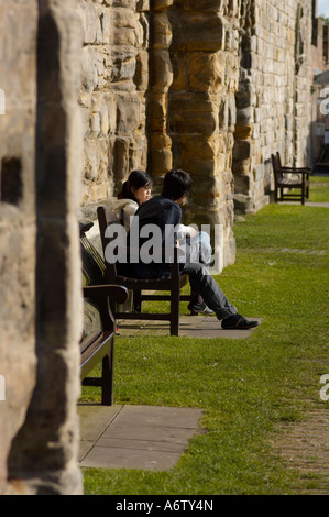 Asian students sitting on a bench in a park in St Andrews Scotland Stock Photo
