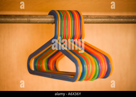 Multi colored plastic clothes hangers in closet, hanging from horizontal bar. Hangers are all very close to one another. Stock Photo