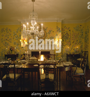 Glass chandelier above table in diningroom with yellow patterned Chinoiserie wallpaper Stock Photo