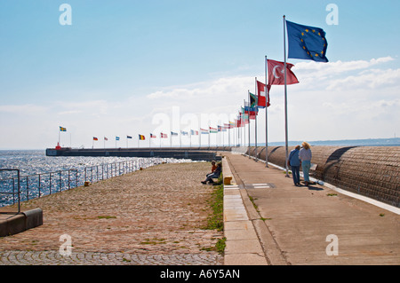 The Pier on Parapeten in the harbour. A long row of national flags flying in the wind. Two people walking. Blue sky. Helsingborg, Skane, Scania. Sweden, Europe. Stock Photo
