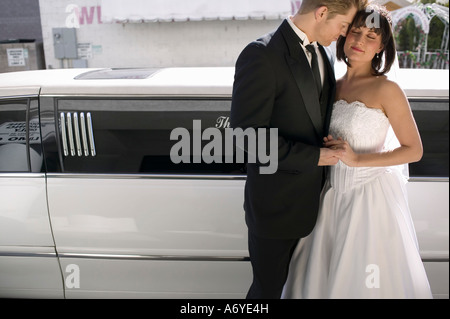 Bride and groom standing together in front of a stretch limousine Stock Photo