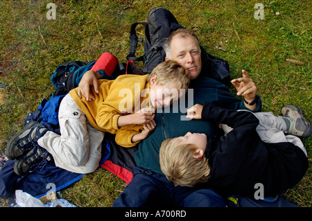 Eight and ten year old boys lying on father at a snack during hiking Stock Photo