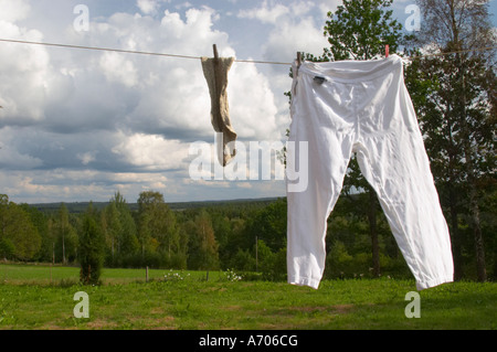 A pair of socks and trousers hanging to dry on a clothes line with clothes pins a summer day with clouds in the sky. Smaland re Stock Photo