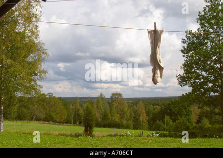 A pair of socks hanging to dry on a clothes line with clothes pins a summer day with clouds in the sky. Smaland region. Sweden, Stock Photo