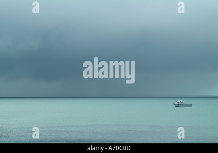 A small boat on a calm ocean with storm clouds above Stock Photo