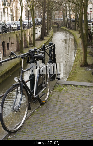Typical Dutch bike parking on the upper bank of Old Canal or Oude Gracht in Utrecht, Holland. A classic bicycle overlooks the historic waterway. Stock Photo