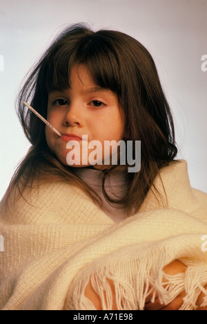 Close up of a young girl with a thermometer in her mouth and wrapped in a blanket Stock Photo