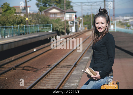 Young woman sitting on suitcase on train platform Stock Photo
