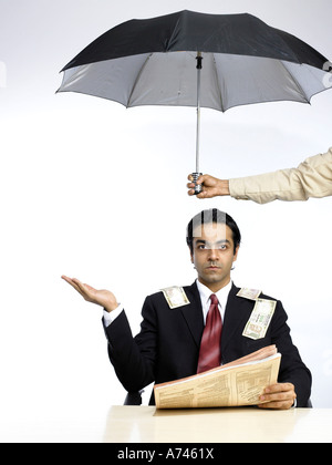VDA 201893 Money fall on South Asian Indian executive extend hand palm up sitting under umbrella MR 702A Stock Photo