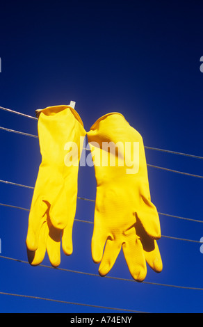 Close up of a pair of bright yellow rubber gloves pegged out to dry on washing-line under deep blue sky Stock Photo